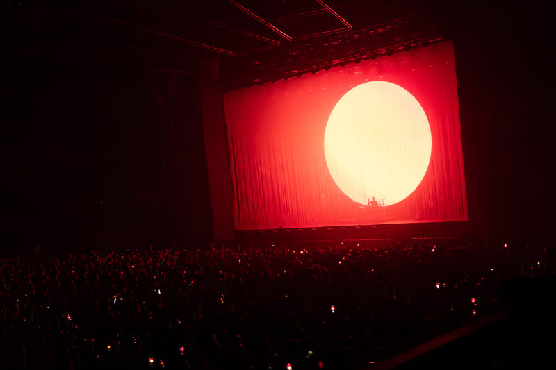 Darkened arena with a glowing disc on a red stage screen above the crowd