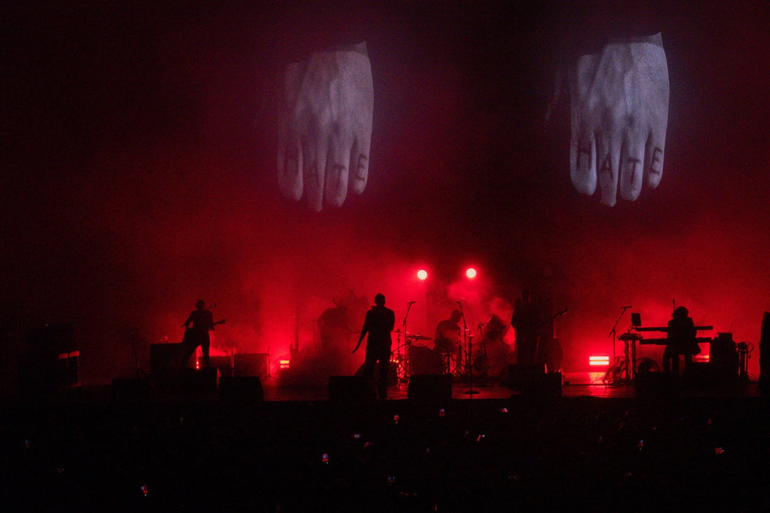 Band in silhouette under red stage lights with giant hand projections