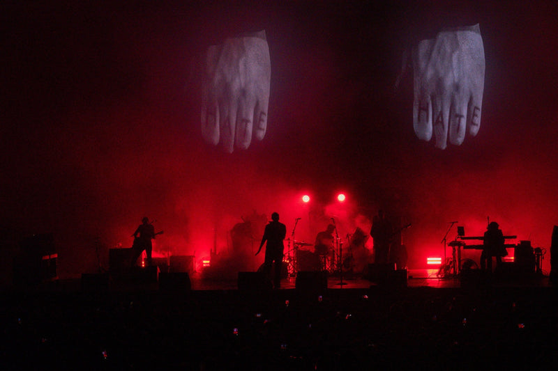 Band in silhouette under red stage lights with giant hand projections