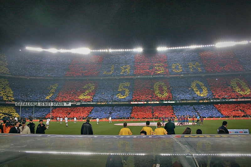 Huge blue, red and yellow card mosaic at Camp Nou at night, seen from pitch level