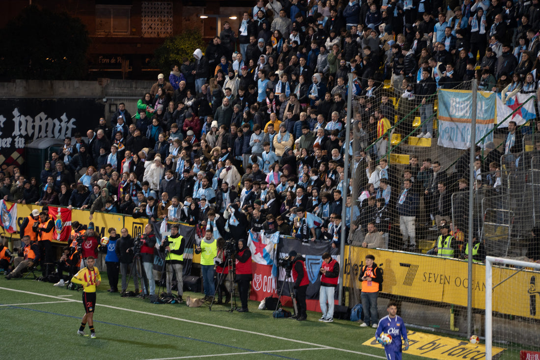 Celta de Vigo supporters in sky-blue scarves fill an away stand at a night match