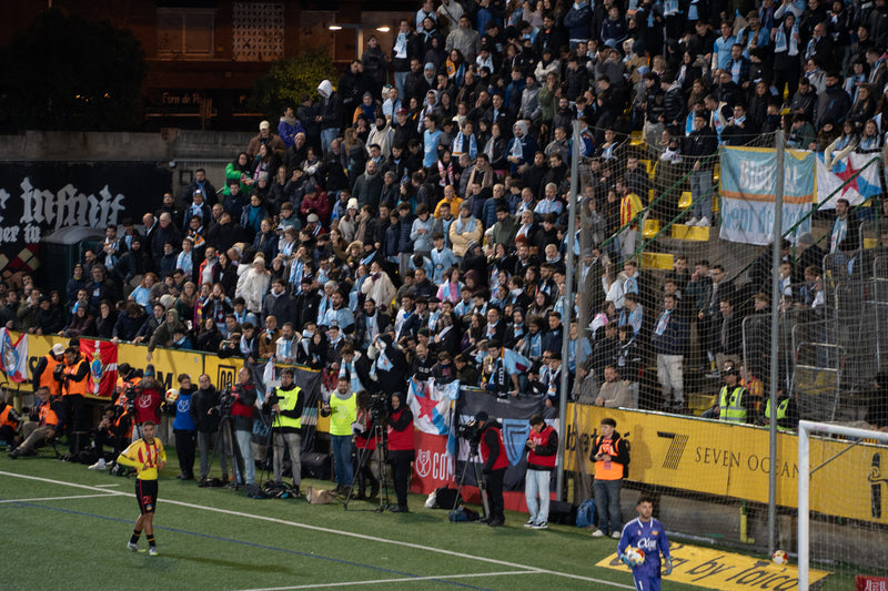 Celta de Vigo supporters in sky-blue scarves fill an away stand at a night match