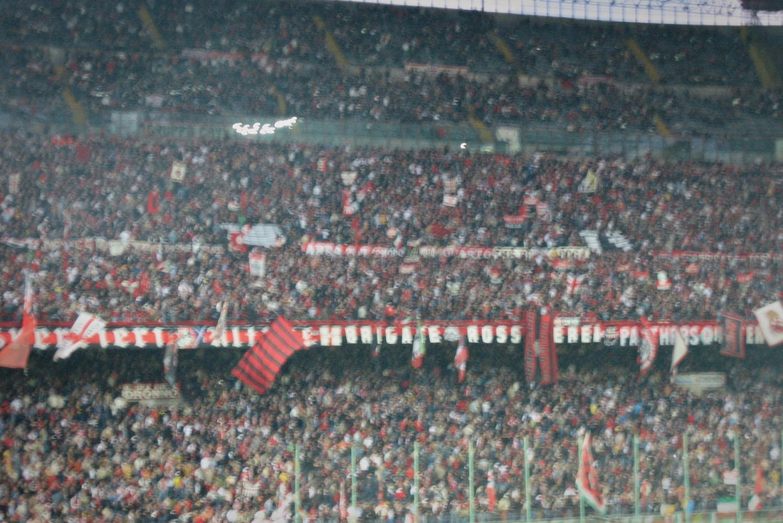 Close, hazy telephoto view of AC Milan supporters in red and black packing a curva at San Siro