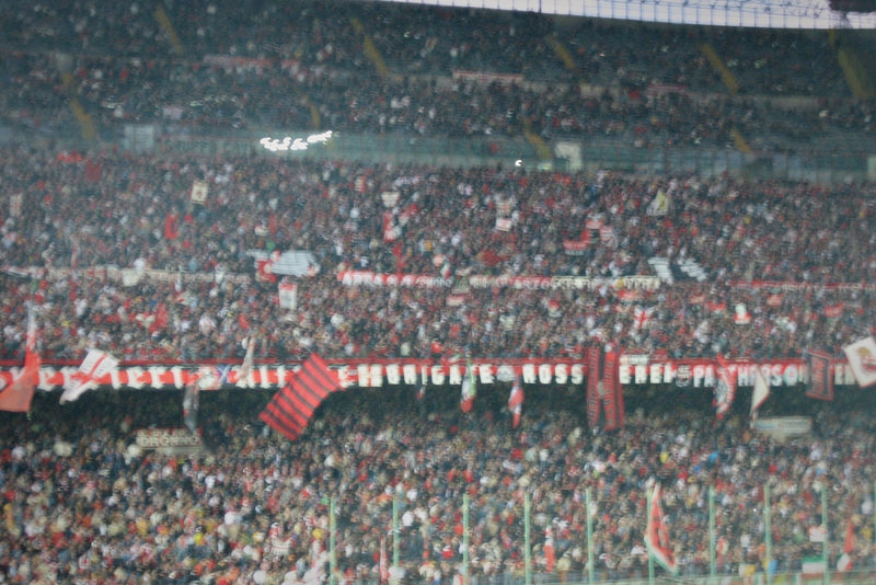 Close, hazy telephoto view of AC Milan supporters in red and black packing a curva at San Siro