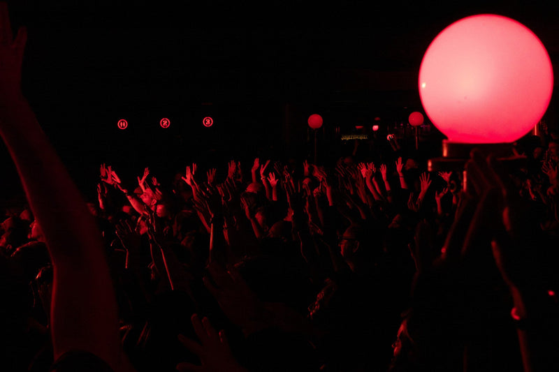 Concert crowd with raised hands beside a large red spherical lamp