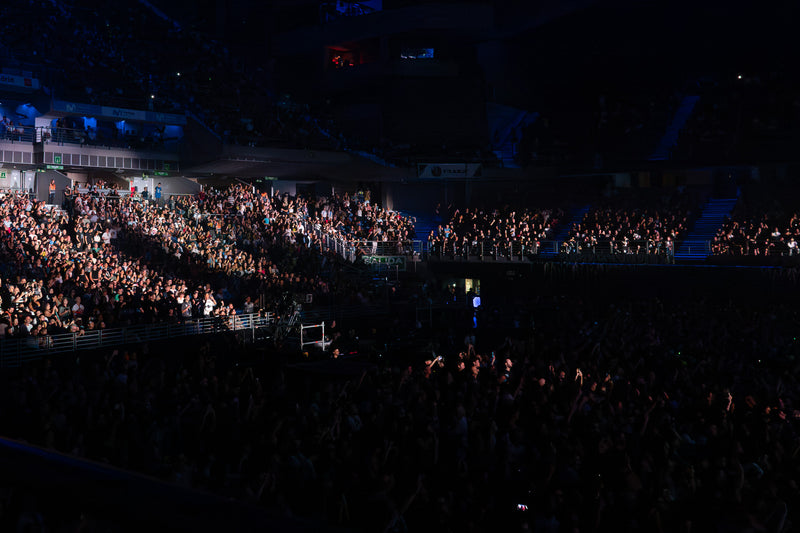 Wide view of a sold-out arena with full seating tiers and a packed floor during a concert