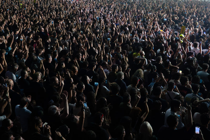 Packed concert crowd seen from above with hundreds of arms raised