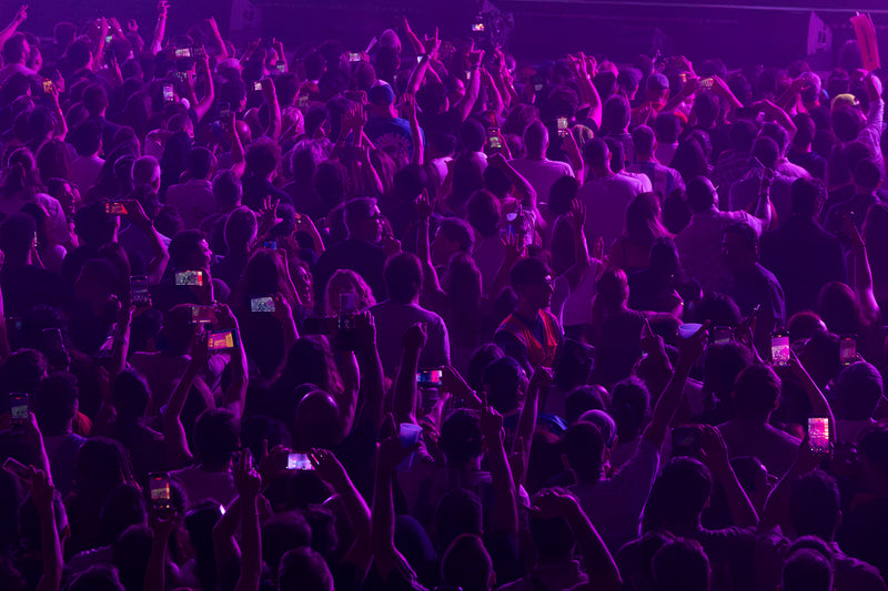 Concert crowd lit in purple holding up phones to film the show