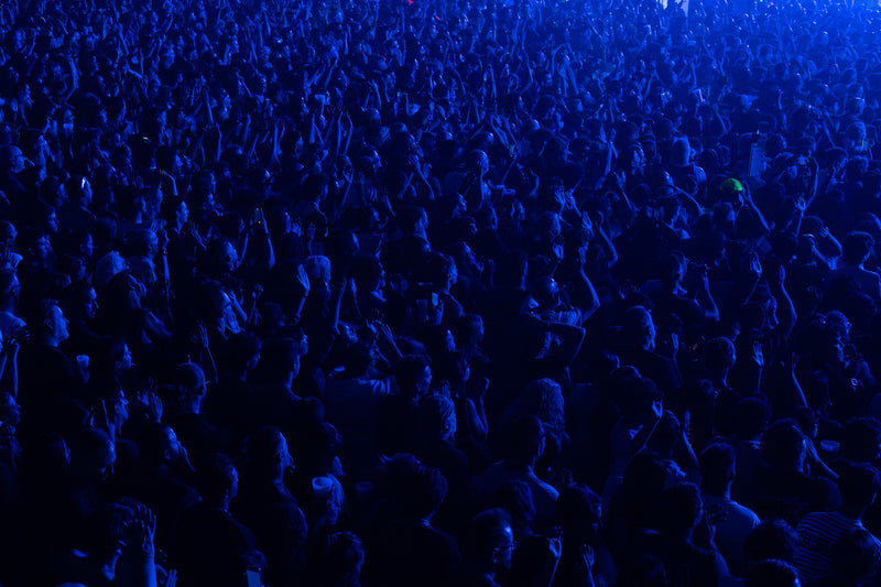 Sea of concert fans with arms raised under deep blue stage lighting
