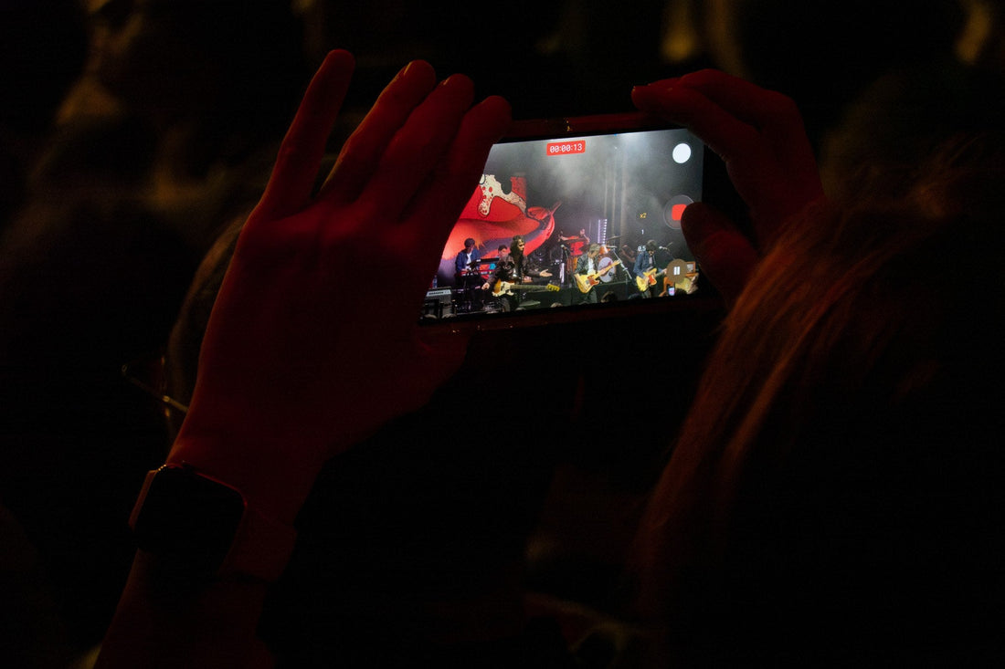Concertgoer filming the stage with a smartphone under red light