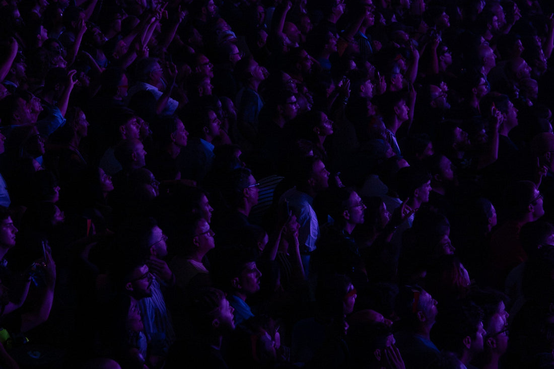 Dense concert crowd lit in magenta and purple raising phones