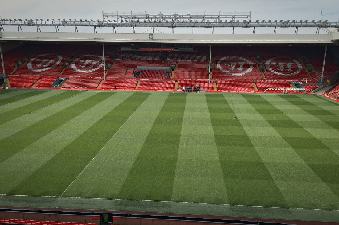 Empty Anfield pitch with striped grass and the red opposite stand on a daytime stadium visit
