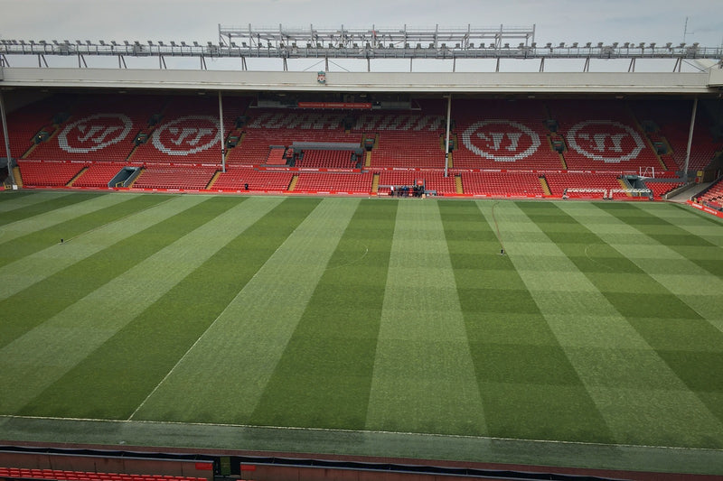 Empty Anfield pitch with striped grass and the red opposite stand on a daytime stadium visit