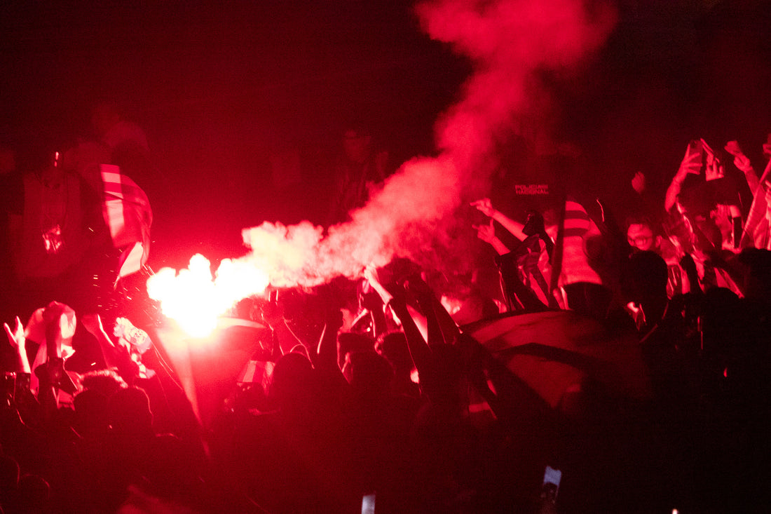 Football supporters light red flares in a packed stand at night