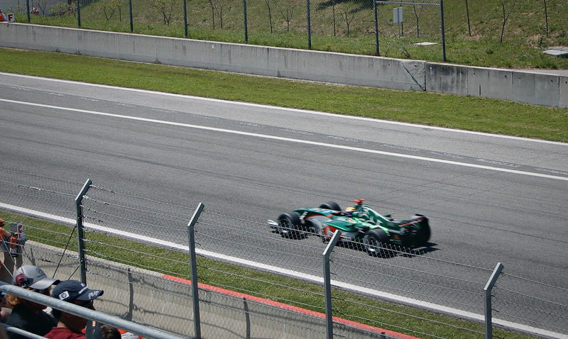Formula 1 car at speed on track behind the catch fence