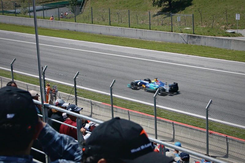 Formula 1 car at speed on track as fans watch from the grandstand behind the catch fence