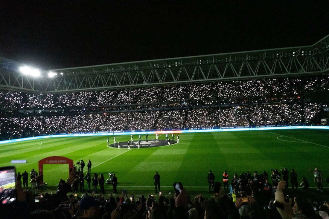 Full stadium bowl at night with both teams lined up at the centre circle