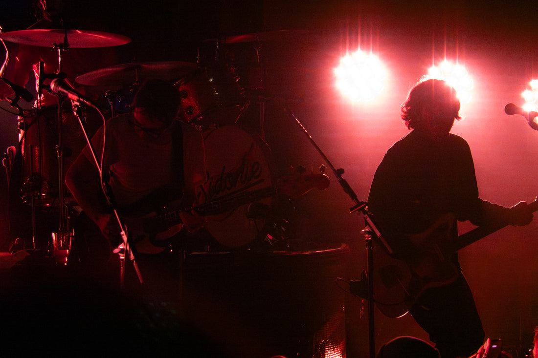 Guitarist and drummer in silhouette under red stage lights at a rock concert