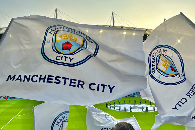 Manchester City supporters waving sky-blue and white flags in the stands