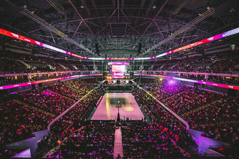 Packed indoor arena lit in pink and purple seen from the upper tier