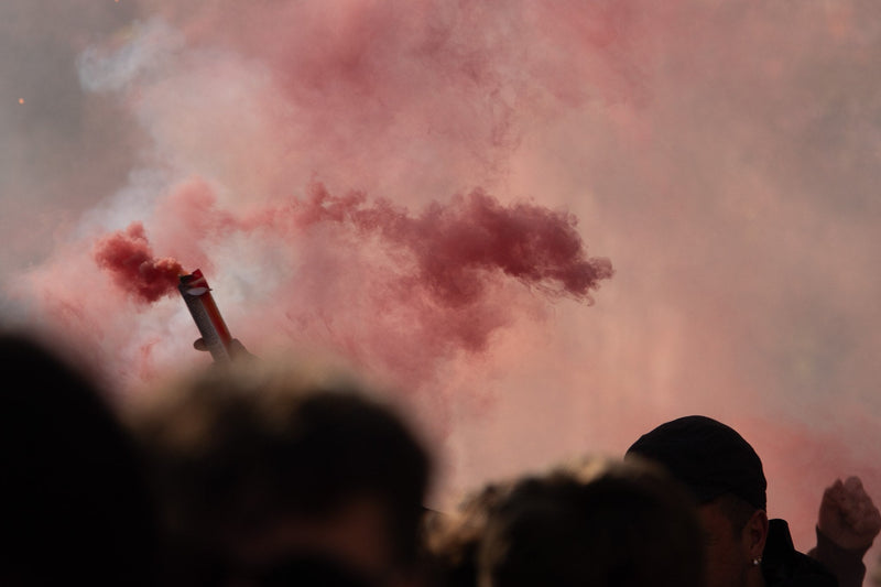 Red flare and smoke drifting over silhouetted fans in a stand