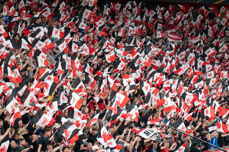 Sea of red-and-black Manchester United flags filling a stand