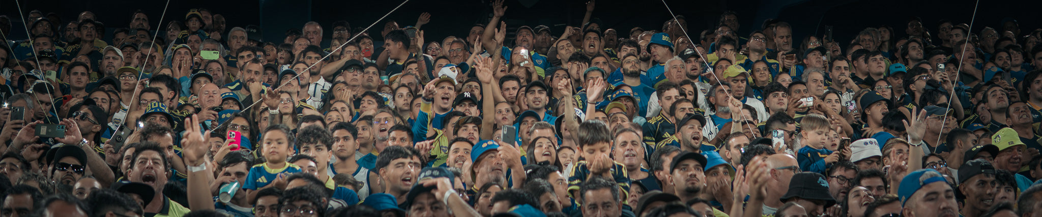 A large crowd of people packed into Boca Juniors Stadium Bombonera , many wearing blue apparel and holding up phones or signs in a crowded football match